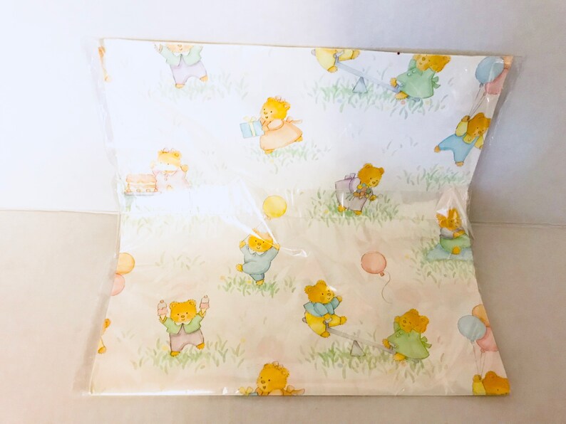 May include: White wrapping paper with a repeating pattern of cartoon bears playing with balloons, a seesaw, and presents. The bears are wearing different colored clothing.