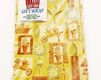 Puede incluir: Un paquete de papel de regalo amarillo y marrón con un tema floral y de jardinería. El papel presenta imágenes de flores, una carretilla y casas para pájaros. El texto en el paquete dice "1/2 Off Card Shop Gift Wrap 2 Sheets Total Each Sheet 20in. x 30in. (50cm. x 76cm.) Distributed by: 1/2 Off Card Shop, Inc. 2,75 €"