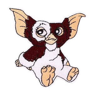 May include: Embroidered patch of a Gremlin character. The patch is in white, brown, and tan. The Gremlin has large ears, big eyes, and a mischievous expression. The patch is designed to be ironed on or sewn onto fabric, suitable for clothing or accessories.