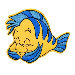 Op de afbeelding: Geborduurde patch met een lachende gele vis met blauwe vinnen en haar. De patch heeft een gedetailleerd ontwerp met zwarte contouren, geschikt voor kleding of accessoires. De vis is een stripfiguur.
