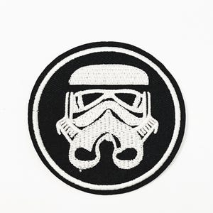 Könnte beinhalten: Schwarzer runder Patch mit weißem Rand, der ein weiß gesticktes Stormtrooper-Helmdesign zeigt.