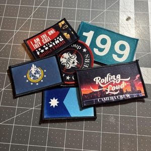 Könnte beinhalten: Eine Sammlung gestickter Aufnäher mit verschiedenen Designs und Texten. Ein Aufnäher lautet: "I AM THE ONE THEY CALL TO KILL THE F***ING BOOGEYMAN." Ein anderer zeigt die Nummer "199." Weitere Aufnäher zeigen Logos und Texte, darunter "Rolling Loud CAMERA CREW."