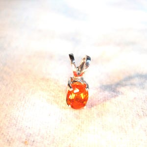 May include: A silver pendant with an orange gemstone. The pendant is oval shaped and has a simple design.