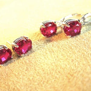 May include: A set of jewelry consisting of two oval-cut, deep pink gemstone stud earrings and two matching oval-cut, deep pink gemstone drop earrings. Each stone is secured in a silver-toned metal setting with four prongs, showcasing a faceted surface.