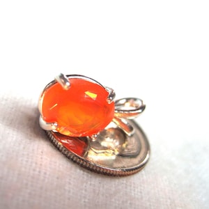 K&ouml;nnte beinhalten: Ein kleiner, orangefarbener Opal-Anh&auml;nger in Silber. Der Anh&auml;nger ist etwa so gro&szlig; wie eine Zehn-Cent-M&uuml;nze.