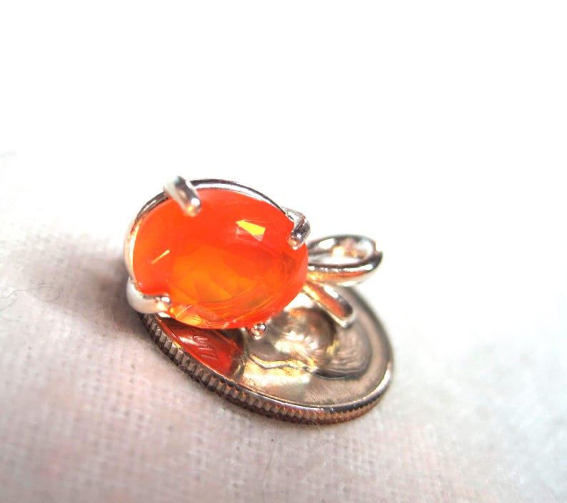 K&ouml;nnte beinhalten: Ein kleiner, orangefarbener Opal-Anh&auml;nger in Silber. Der Anh&auml;nger ist etwa so gro&szlig; wie eine Zehn-Cent-M&uuml;nze.
