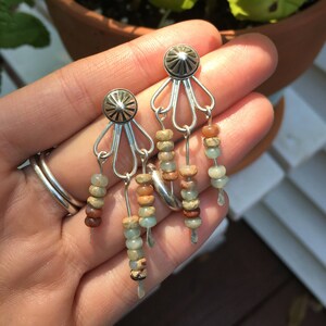 May include: Silver dangle earrings with a silver starburst design and multiple strands of brown, green, and beige beads.