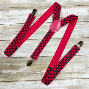 May include: Red suspenders with black and white checkered pattern. The suspenders have silver clips and a pink leather button.