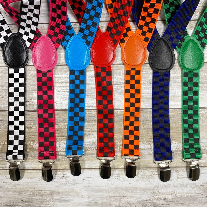 May include: Eight pairs of suspenders with checkered patterns in various colors, including black and white, black and red, black and blue, black and orange, black and green, and black and navy blue. The suspenders have silver clips and leather adjustable straps.