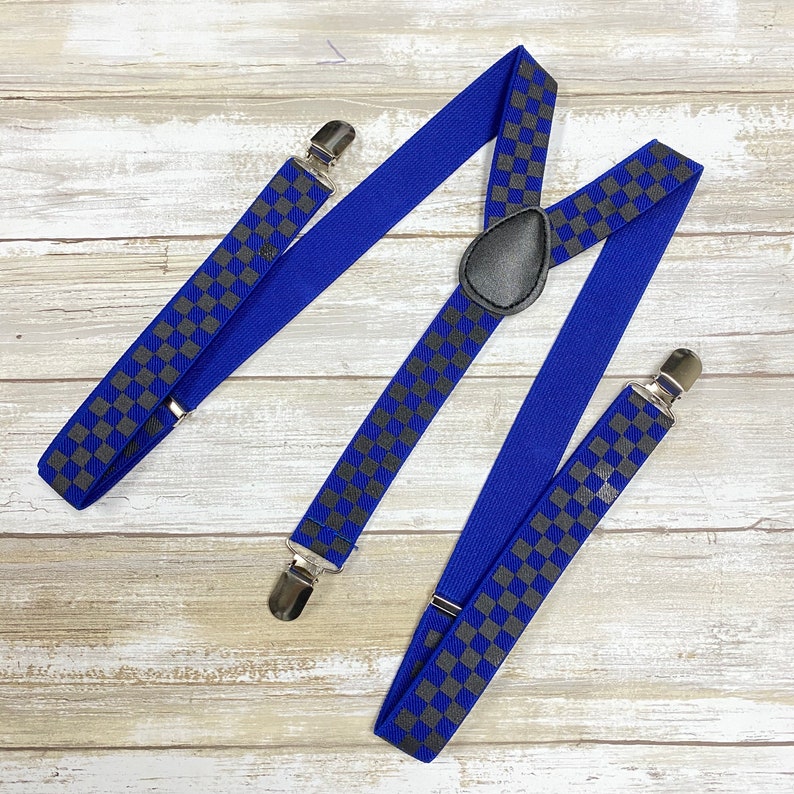 May include: Blue suspenders with a checkered pattern in gray. The suspenders have silver clips and a silver adjustable buckle.