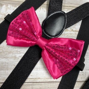 Könnte beinhalten: Rosa Schleife mit Pailletten auf schwarzen Hosenträgern. Die Schleife ist aus Satin und hat eine Schicht Tüll mit Pailletten darüber.