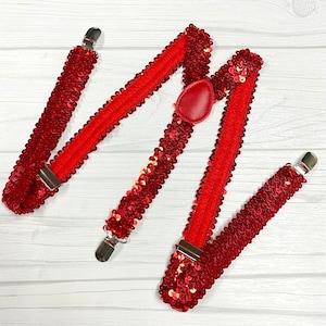 May include: Red sequined suspenders with silver clips and a red button.