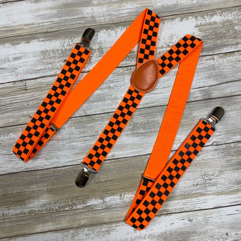 May include: Orange suspenders with black checkered pattern. The suspenders have adjustable straps and metal clips.