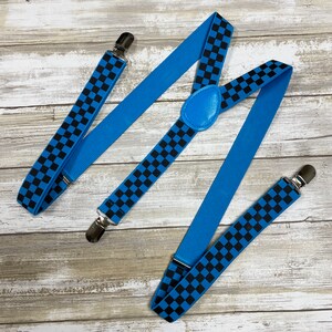 May include: Blue suspenders with a black and white checkered pattern. The suspenders have silver clips and a blue leather adjustable strap.