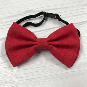 May include: A red bow tie with an adjustable elastic strap. The bow tie is made of a textured fabric.