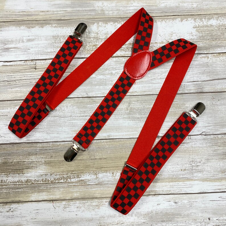 May include: Red suspenders with black checkered pattern. The suspenders have silver clips and a red leather adjustable strap.