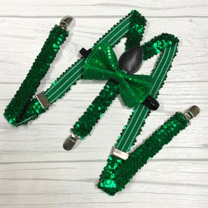 Può includere: Bretelle di paillettes verdi con papillon abbinato. Le bretelle hanno strisce bianche e clip argentate. Il papillon è realizzato in paillettes verdi e ha un retro in feltro nero.
