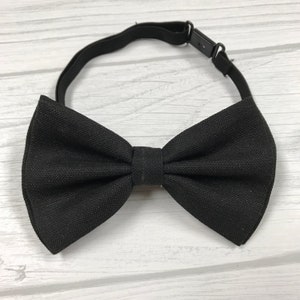 May include: A black bow tie made of a textured fabric with an adjustable elastic strap.