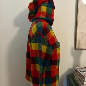 May include: A hooded fleece jacket in a vibrant plaid pattern of red, yellow, green, and blue. The jacket has a front pocket and a matching hood. The garment is displayed on a mannequin.