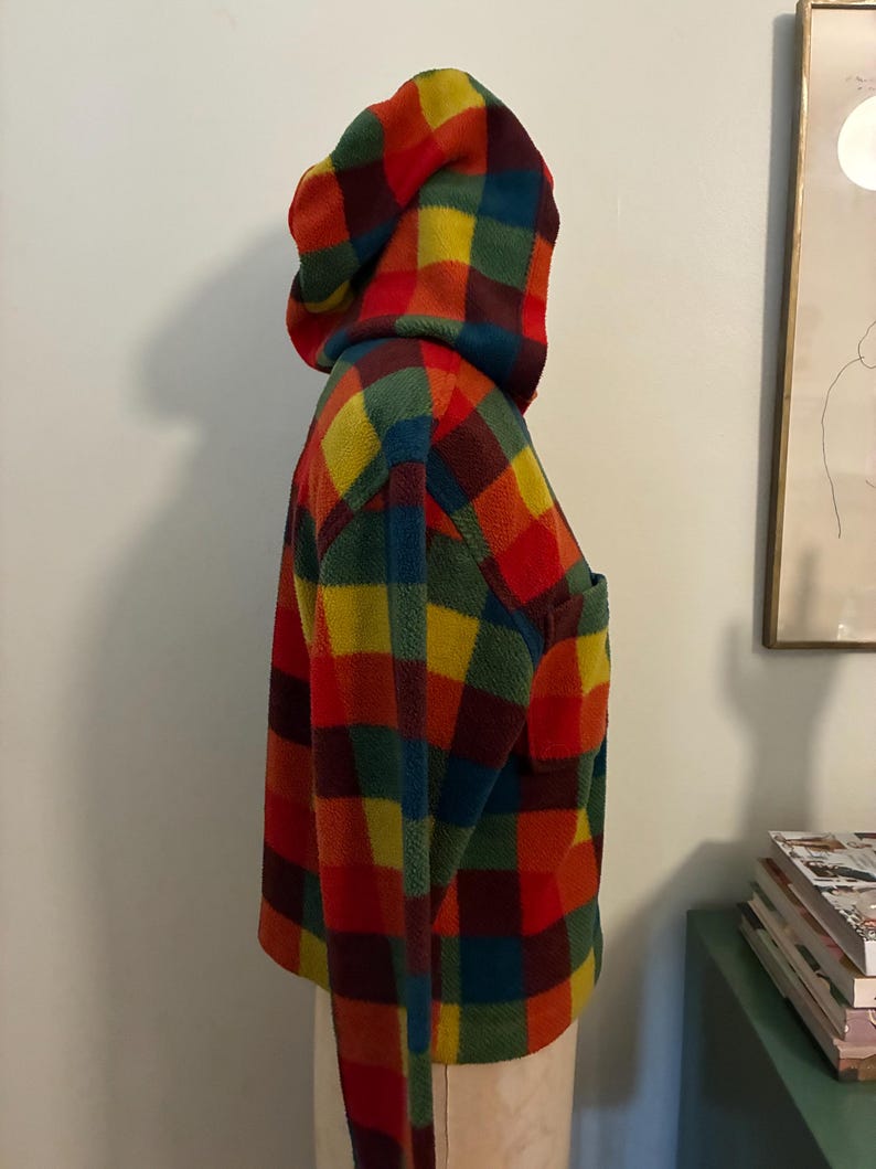 May include: A hooded fleece jacket in a vibrant plaid pattern of red, yellow, green, and blue. The jacket has a front pocket and a matching hood. The garment is displayed on a mannequin.