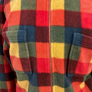 May include: A colorful, vintage fleece jacket with a plaid pattern in shades of red, orange, yellow, green, and blue. The jacket has a full zipper closure and two front pockets. The fabric appears soft and plush.