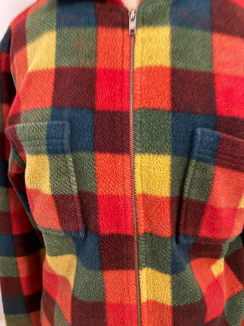 May include: A colorful, vintage fleece jacket with a plaid pattern in shades of red, orange, yellow, green, and blue. The jacket has a full zipper closure and two front pockets. The fabric appears soft and plush.
