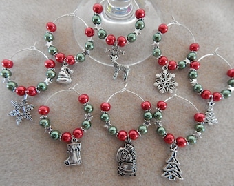 May include: Six Christmas-themed wine glass charms with red and green beads and silver charms. The charms include a snowflake, a stocking, a Christmas tree, a Santa Claus, a reindeer, and a Santa hat.