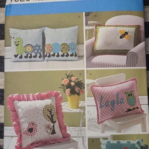May include: Simplicity 1929 pillow sewing pattern. The pattern features various pillow designs, including a caterpillar, a heart with a bee, an owl, and a bird with a tree. The pattern is one size and includes the text "giggles and toots".