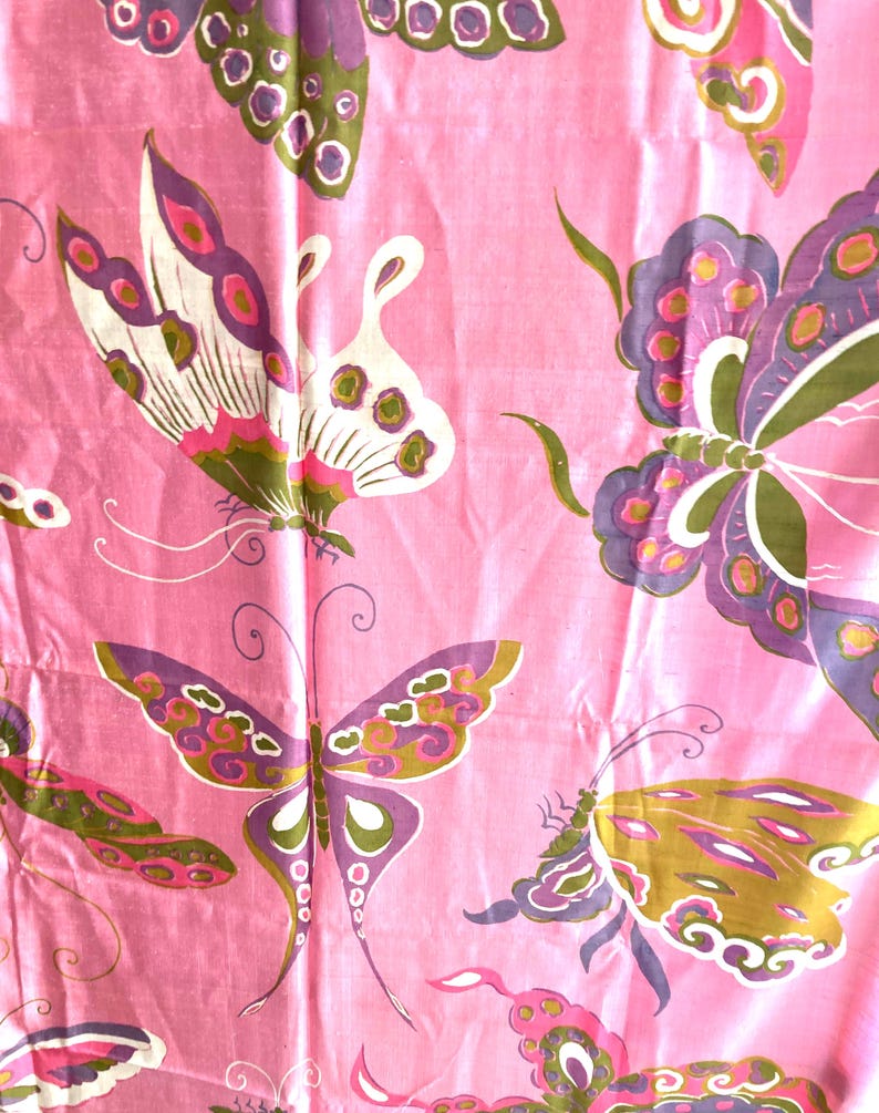 May include: A pink fabric featuring a repeating pattern of butterflies in shades of purple, olive green, and white. The butterflies are depicted with detailed wing markings and long antennae, distributed across the surface of the textile.