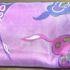 May include: A folded fabric square featuring a vibrant pink base color with a repeating pattern of abstract floral shapes in shades of purple, blue, olive green, and white. The material has a subtle sheen and a smooth, woven texture throughout.