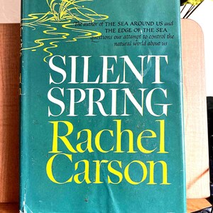 May include: A vintage book titled "Silent Spring" by Rachel Carson. The cover is teal with yellow lettering and a yellow illustration. The text includes the author's name and a quote about the natural world.