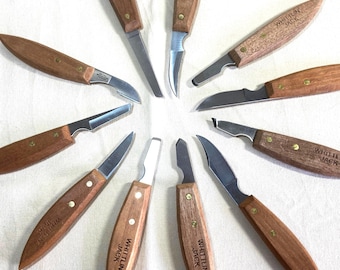 May include: A collection of wood carving knives arranged in a circular pattern. Each knife features a wooden handle, a silver blade, and the text "WHITTLIN JACK" printed on the handle. The knives are designed for detailed wood carving.