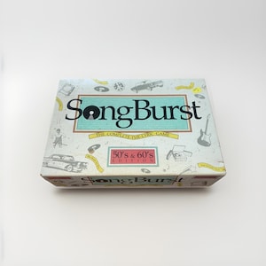 May include: A SongBurst board game box with a light blue background and vintage-style illustrations. The box features the text "SongBurst" in large letters, with "50's & 60's Edition" below. The game is "The Complete Lyric Game".