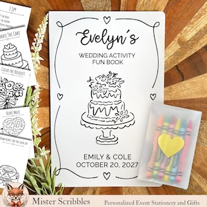 May include: A white wedding activity fun book with black line art of a tiered cake, hearts, and the text Evelyn's Wedding Activity Fun Book, Emily & Cole, October 20, 2027. Includes a small translucent pouch containing five colorful wax crayons.