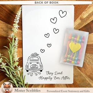 May include: A white rectangular activity book with a black line drawing of a car with a Just Married sign and trailing cans, accompanied by floating hearts and the text They Lived Happily Ever After, plus a small clear pouch containing six crayons.