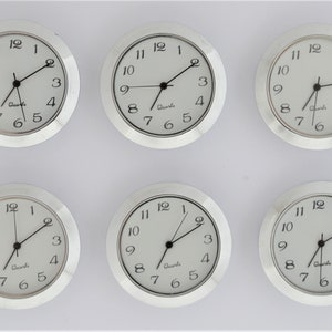 May include: Six silver-colored analog clocks with white faces and black hands. Each clock has a black rim and black numbers. The clocks are arranged in two rows of three.