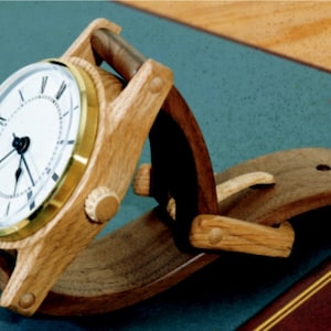 Könnte beinhalten: Ein Uhrenständer aus Holz mit hellbrauner Oberfläche. Der Ständer ist so konzipiert, dass er eine Armbanduhr in vertikaler Position hält. Der Ständer besteht aus zwei Holzstücken, die mit einem Scharnier verbunden sind. Der Uhrenständer ist eine einzigartige und stilvolle Möglichkeit, eine Armbanduhr zu präsentieren.