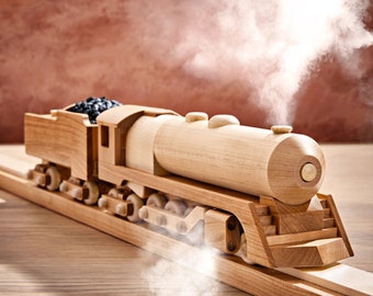 May include: A wooden toy train engine with a black coal car, on a wooden track, with steam coming out of the engine.