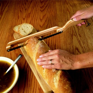 May include: A wooden bread knife with a serrated blade is used to slice a loaf of bread on a wooden cutting board.