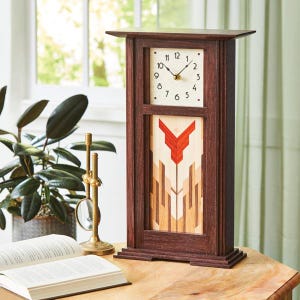 May include: A dark brown wooden mantel clock with a rectangular face and a decorative floral design. The clock face has black numbers and hands. The lower section features a red and beige geometric pattern. The clock sits on a wooden table.