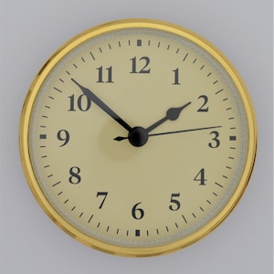 May include: A gold-colored clock face with black numbers and hands. The clock face is set to 10:10.