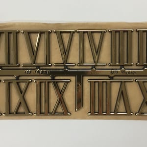 May include: A set of gold Roman numeral clock numbers. The numbers are arranged in two rows, with the numbers I through XII in the top row and the numbers XIII through XXIV in the bottom row.