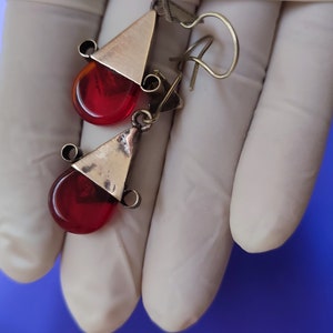 May include: A pair of earrings with red glass teardrop-shaped stones and silver triangle accents.