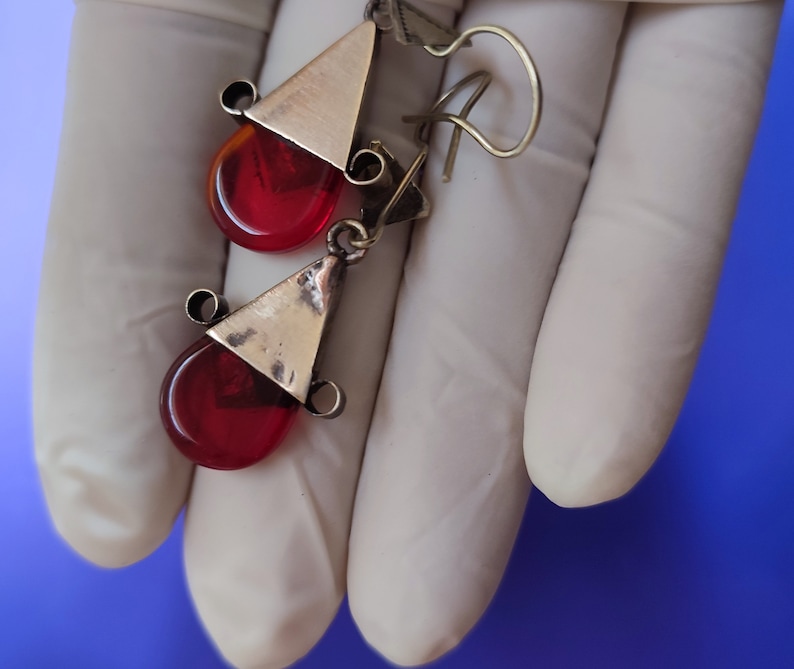 May include: A pair of earrings with red glass teardrop-shaped stones and silver triangle accents.