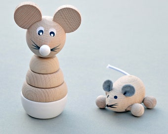 May include: Two wooden toy mice. One is a stacking toy with a white base and a mouse head. The other is a small mouse with gray ears and a white tail. Both toys are made of light-colored wood.