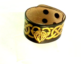 May include: Black leather bracelet with a gold Celtic knot design.