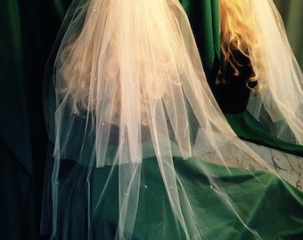 May include: A white tulle bridal veil with a single-tier design and scattered pearl embellishments. The veil is displayed on a green background.