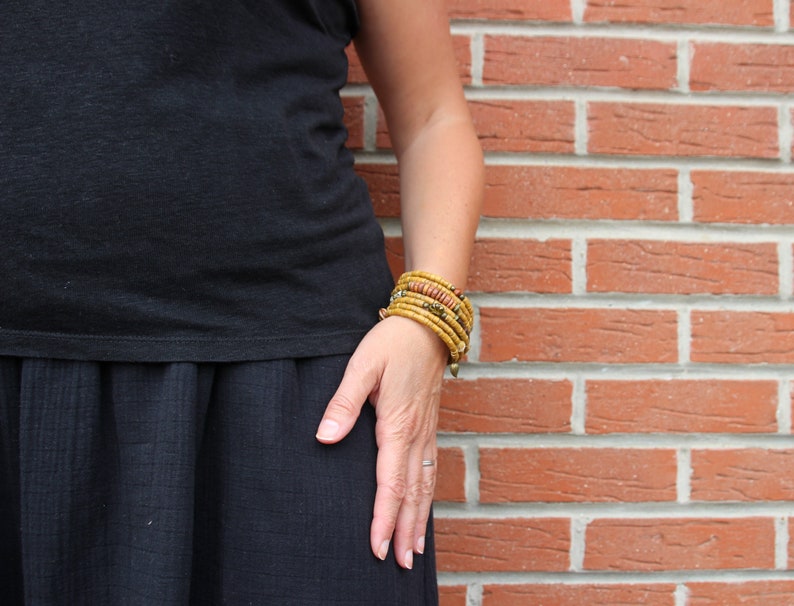 May include: A person wearing a black top and skirt with multiple yellow and orange beaded bracelets on their wrist.