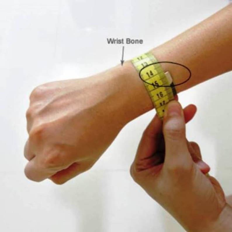 Puede incluir: Una cinta m&eacute;trica amarilla est&aacute; envuelta alrededor de la mu&ntilde;eca de una persona para medir el hueso de la mu&ntilde;eca. La cinta lee "14" y "15". El texto "Wrist Bone" est&aacute; escrito sobre la mu&ntilde;eca.