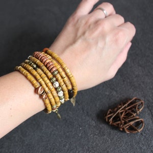 May include: A stack of yellow, brown, and white beaded bracelets on a person's wrist. The bracelets are made of natural materials and have a rustic, bohemian style.